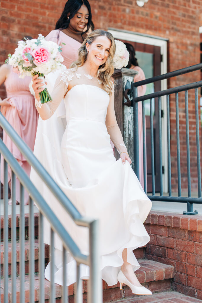 a wedding photograph of a bride with bouquet coming down the stairs with her bridesmaids photographed by rachael and jacob who take luxury wedding photos