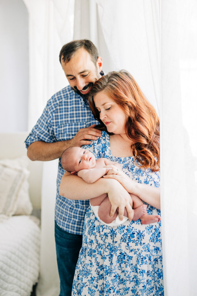 Father and mother posing with newborn in bedroom during a lifestyle session