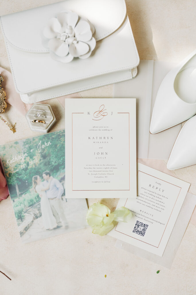 Flat lay board of wedding invite, wedding rings, invitation and bridal shoes and purse.