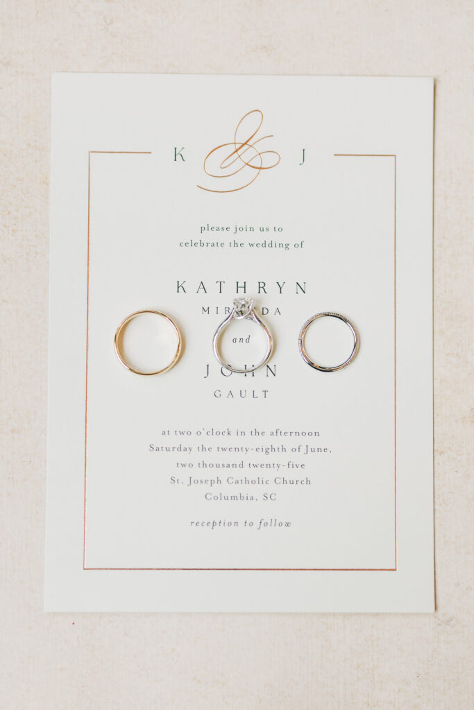 Close up of wedding rings and invitation on flat lay board.