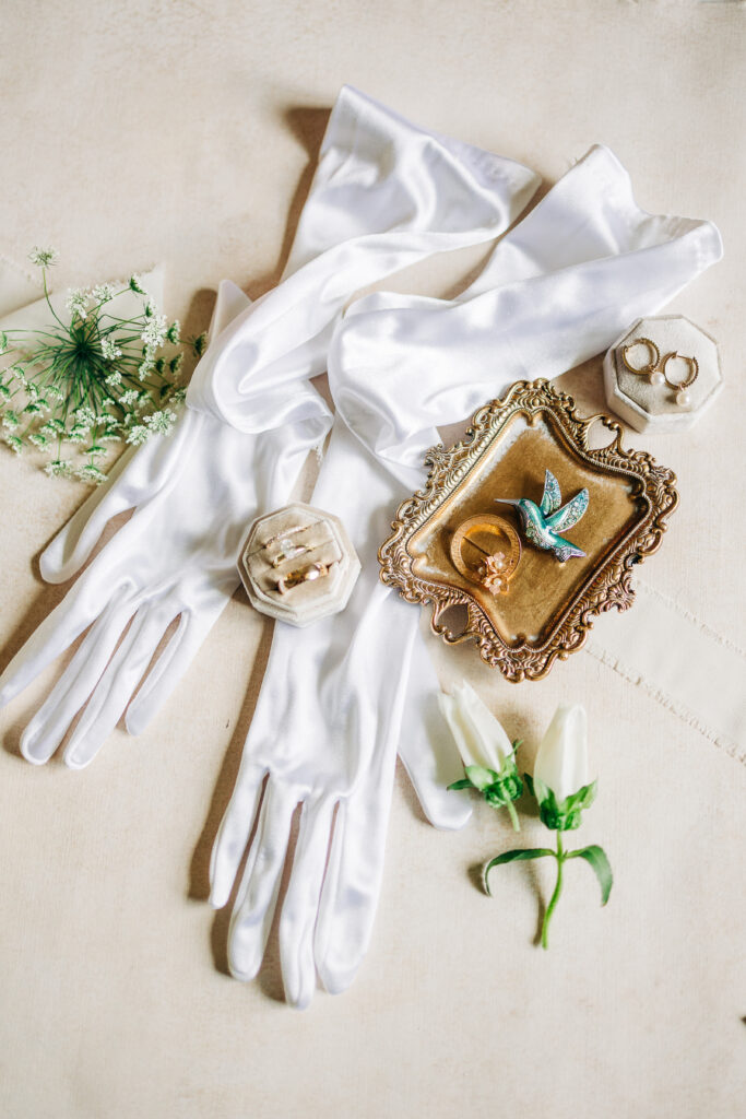 Wedding rings styled with silk wedding gloves on flat lay board.