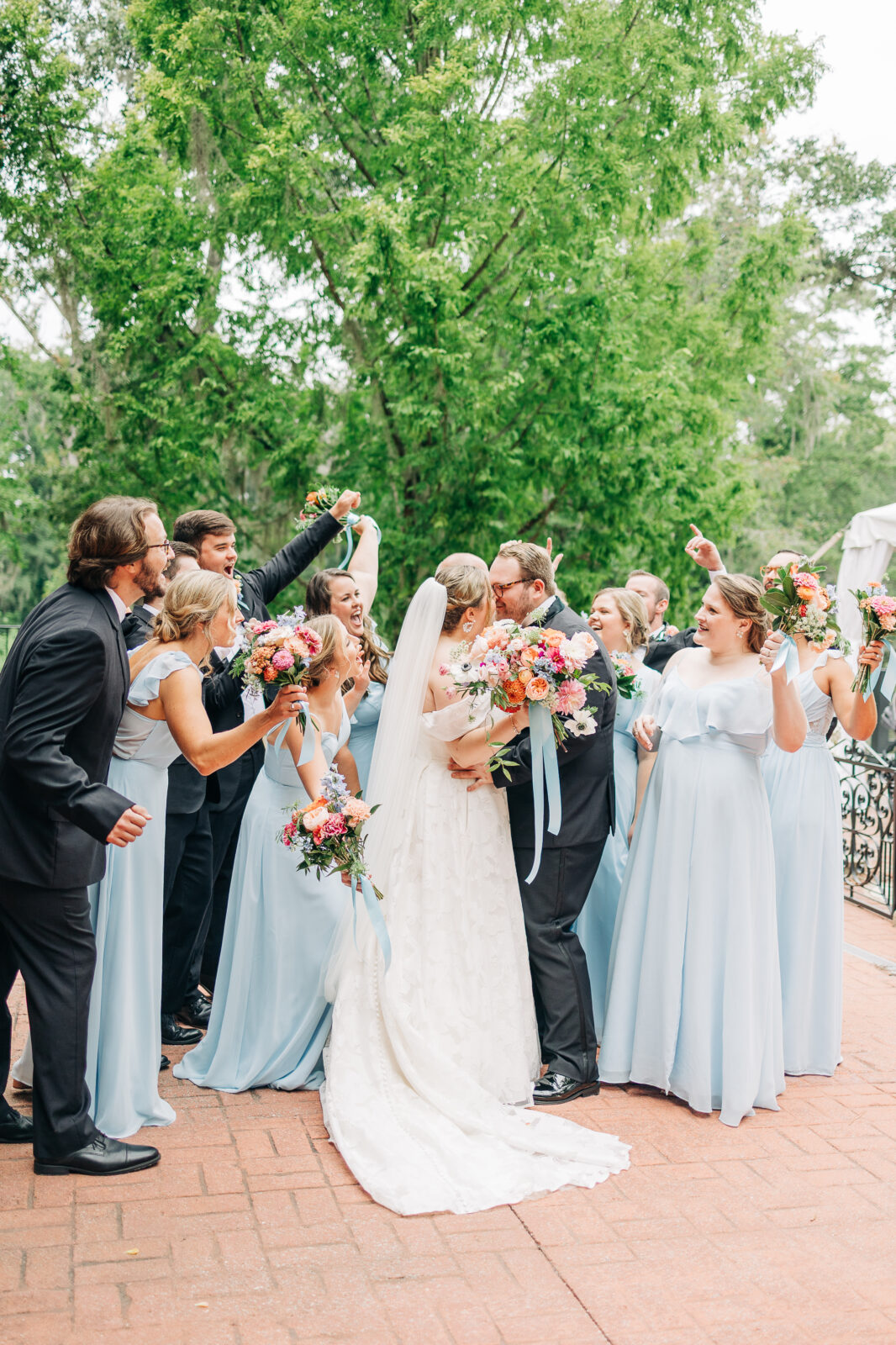 A candid and fun wedding party photo with the couple kissing in the South Carolina center and their friends celebrating