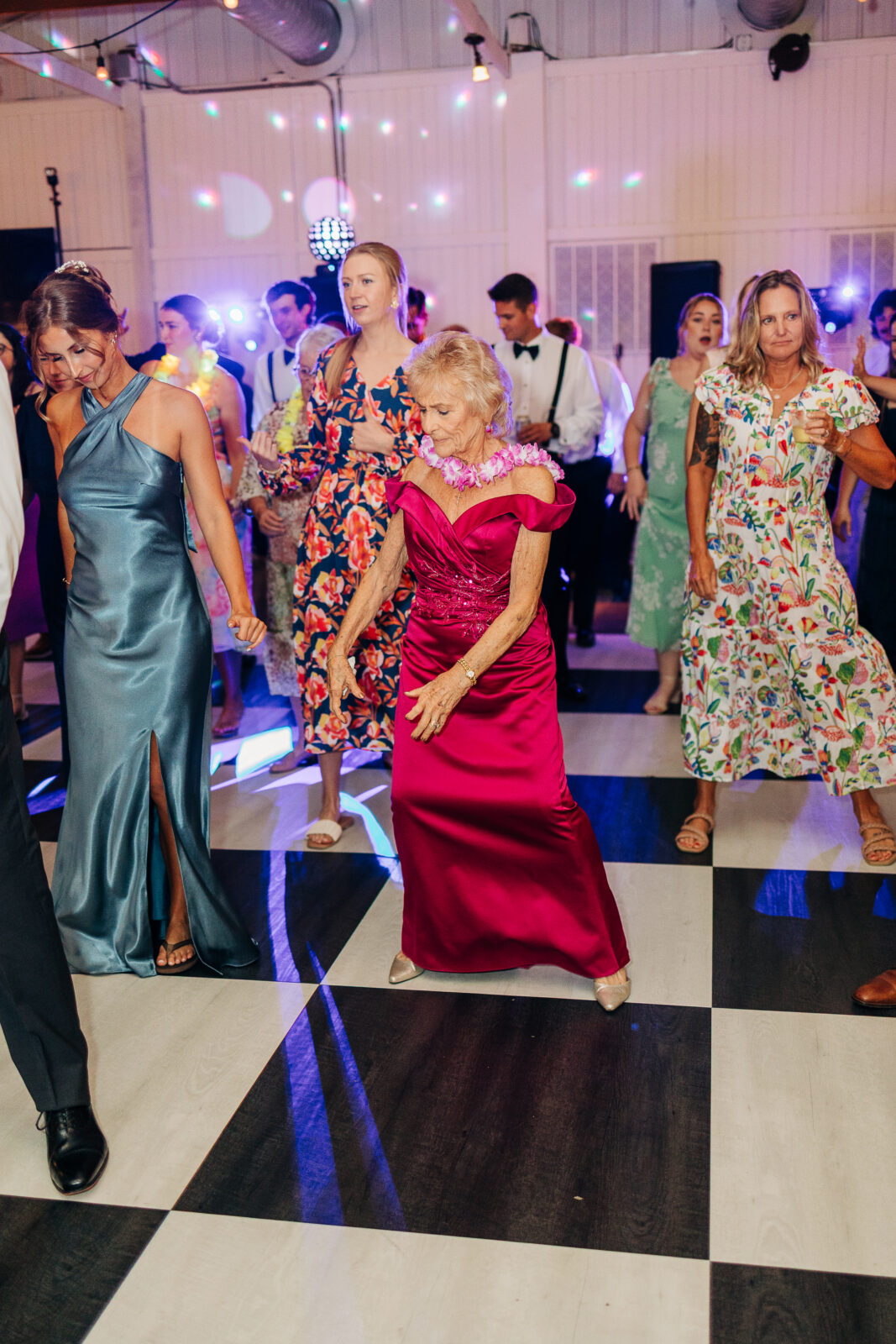 A candid photo of a woman in a pink dress and a floral lei dancing at a wedding reception