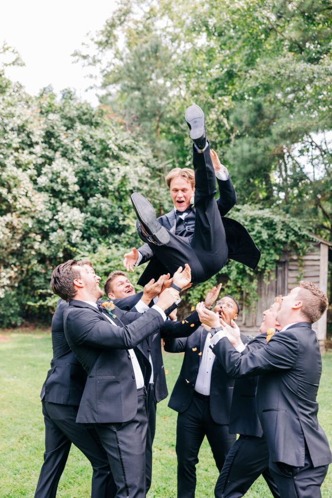 Candid wedding photo of the groom being lifted in the air by his groomsmen