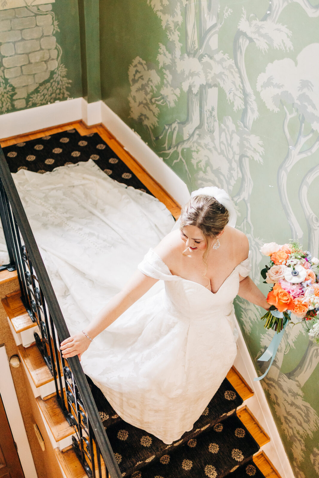 Bride in off-shoulder gown holding colorful bouquet walking down staircase before Columbia wedding ceremony