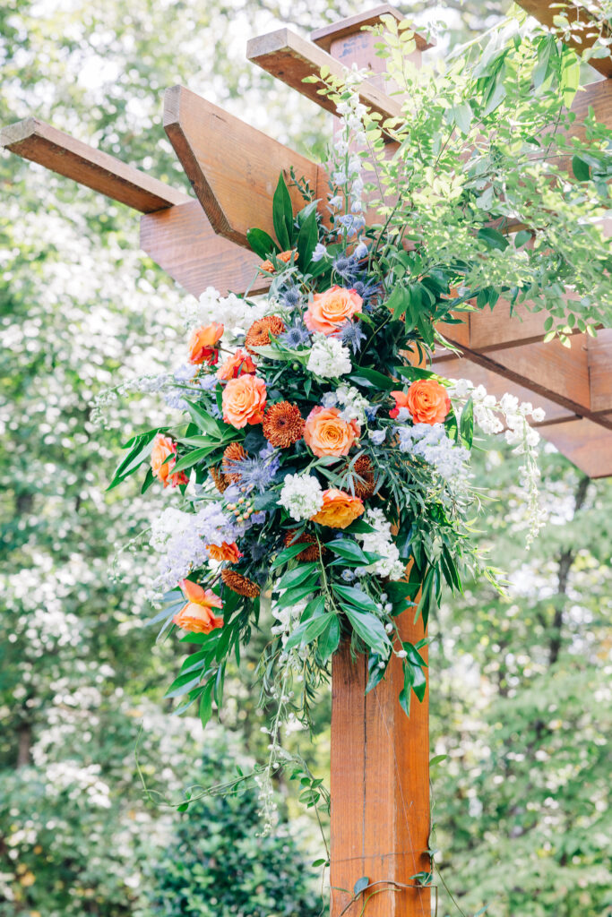 A wedding arbor decorated with a beautiful arrangement of flowers, including orange and white roses