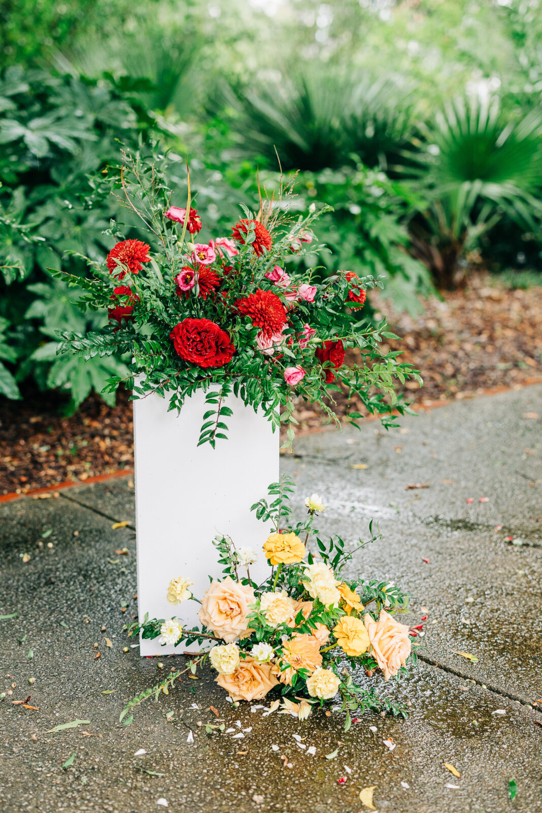
Lush red and pink ceremony flowers in white stand with yellow and orange roses on the ground, Hampton-Preston Mansion