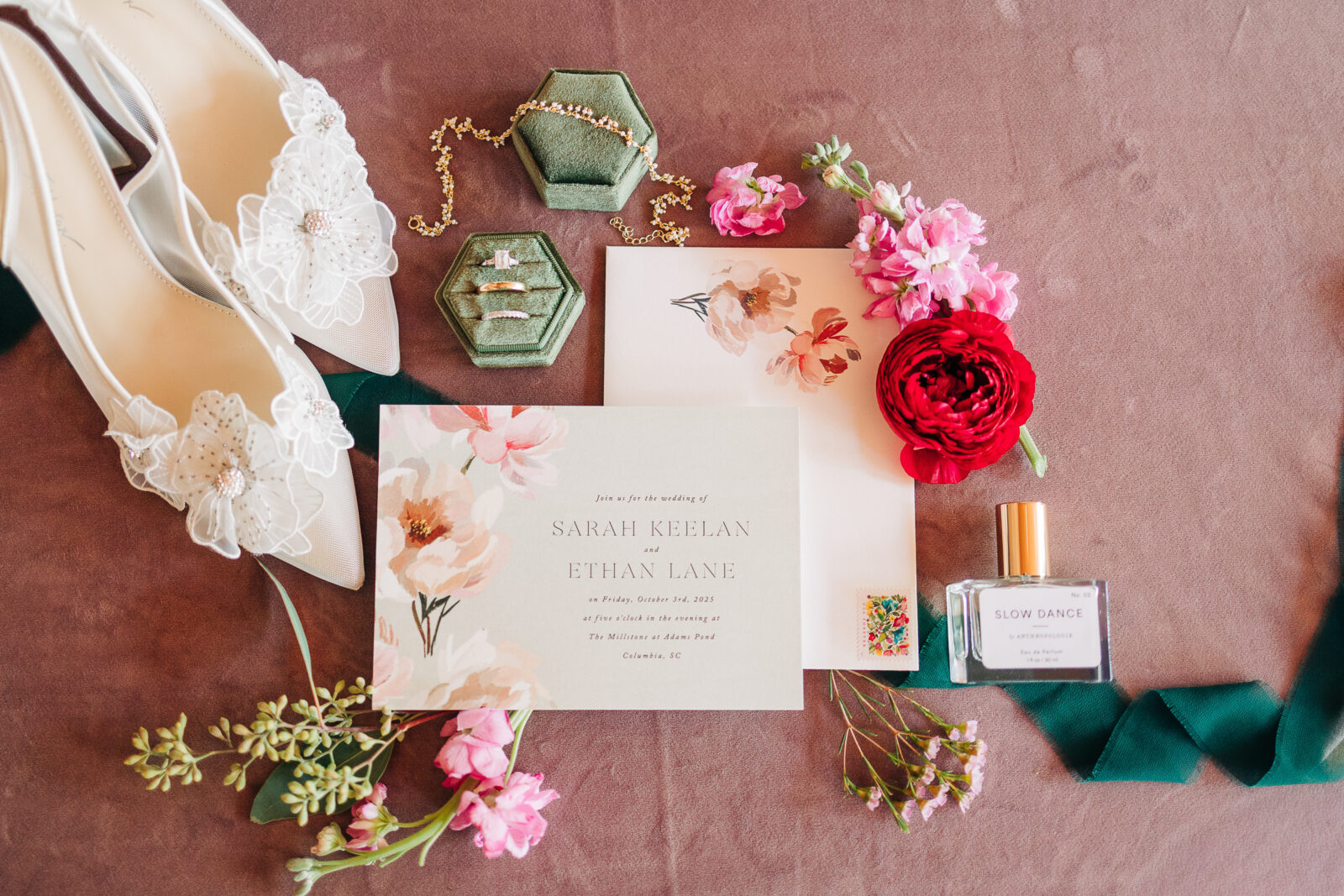 Styled flat lay of the Millstone at Adams Pond wedding invitation suite, bridal shoes, and rings on a pink velvet background