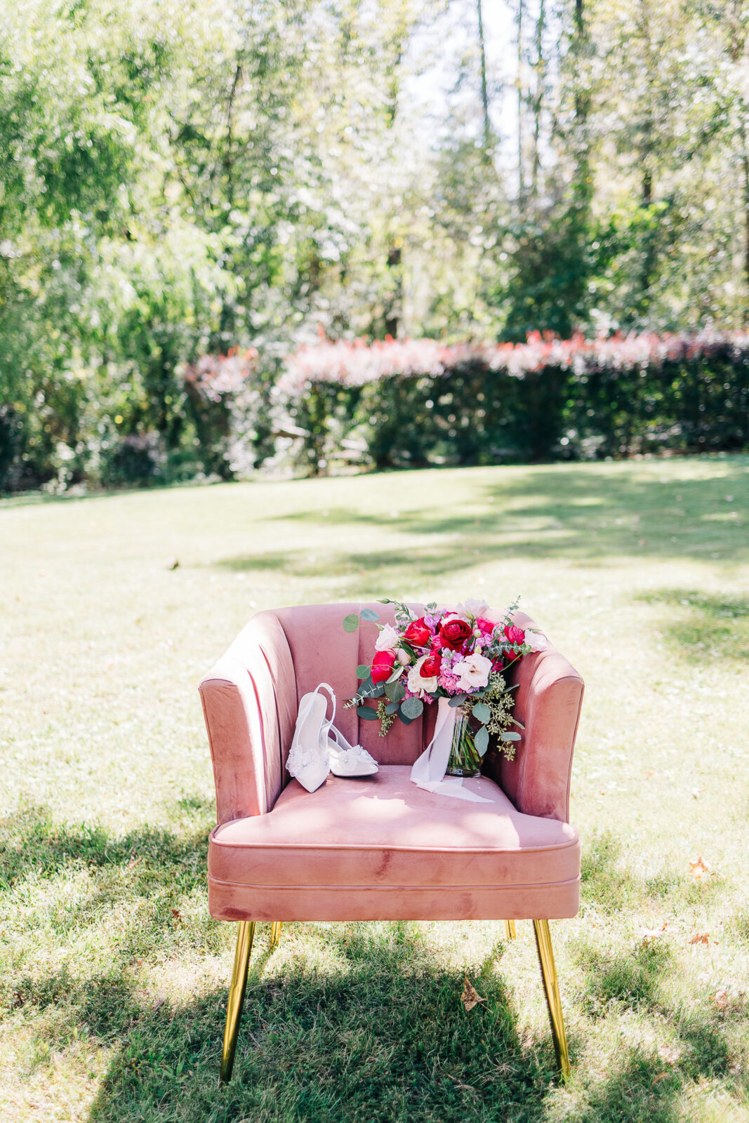 Bright bridal bouquet of red roses, pink flowers, and white shoes on a blush velvet chair for a wedding in Columbia, SC