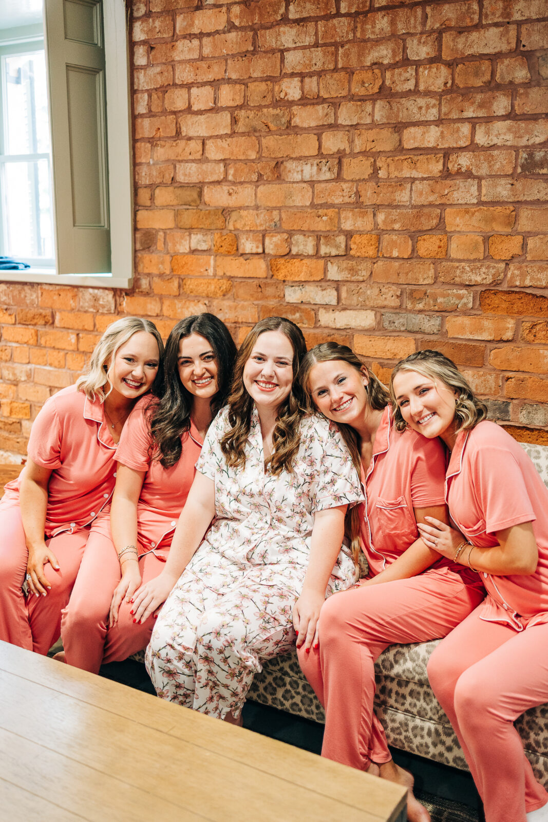 Bride and bridesmaids in pajamas smiling for a getting ready portrait against a brick wall in Columbia, SC