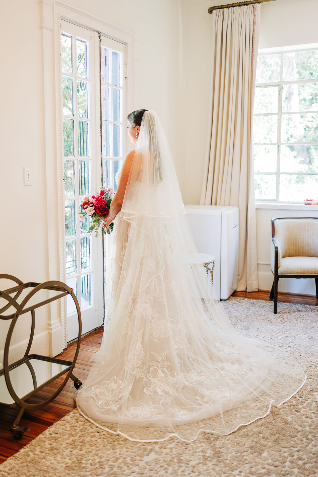 Bride full length portrait looking out a large window, showing the long train and veil of her lace wedding dress at The Millstone at Adams Pond