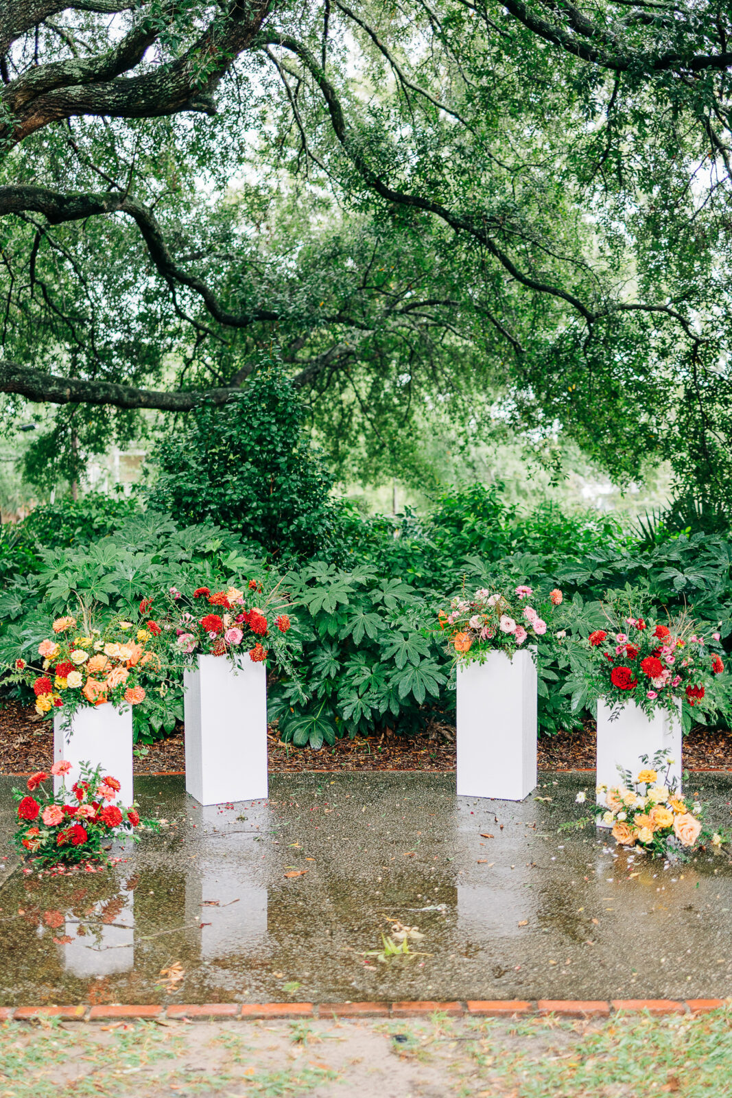 Four vibrant floral arrangements in white planters marking the ceremony space under a lush tree canopy at Hampton-Preston Mansion and Gardens in Columbia, SC