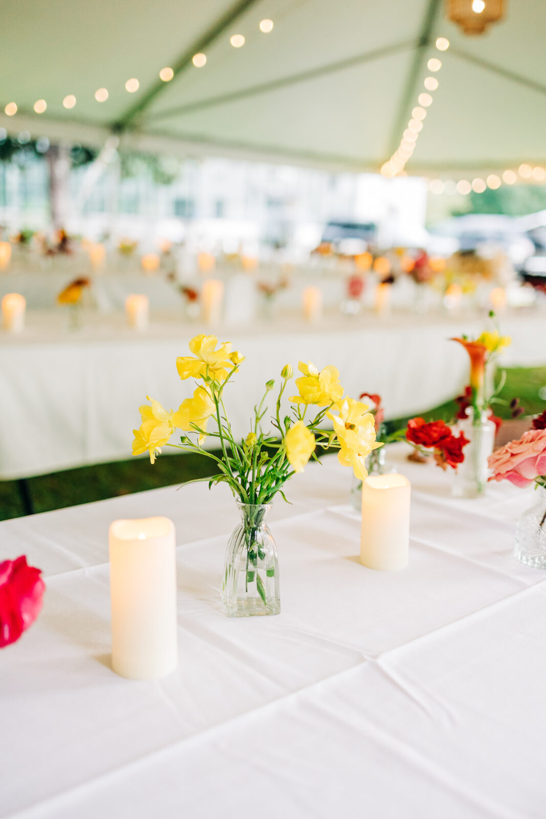 Close-up of a reception table centerpiece with yellow flowers and pillar candles under a string-lit tent at a Hampton-Preston Mansion wedding in Columbia, SC