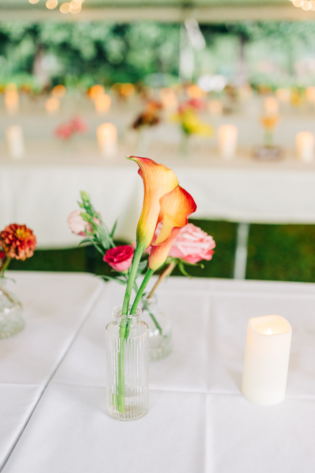 Close-up of orange and yellow calla lily centerpiece and pillar candle on a white tablecloth at a Hampton-Preston Mansion wedding reception