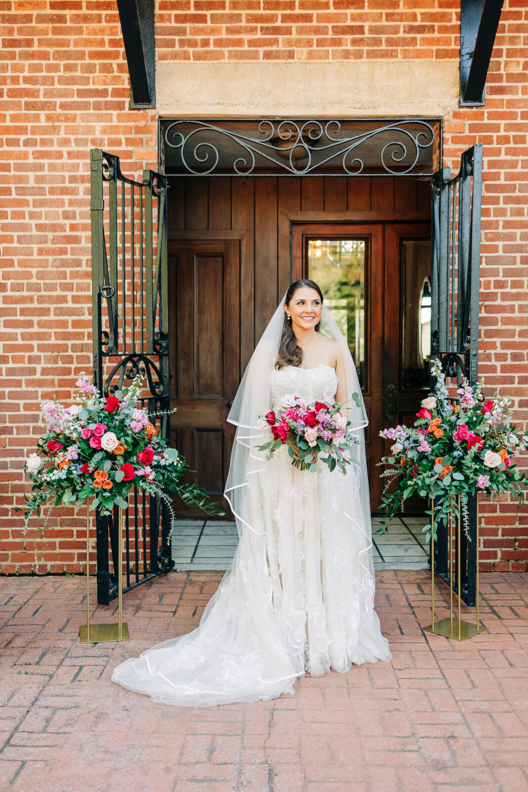 Stunning outdoor bridal portrait featuring a bright pink, red, and orange floral arrangement at a historic wedding venue