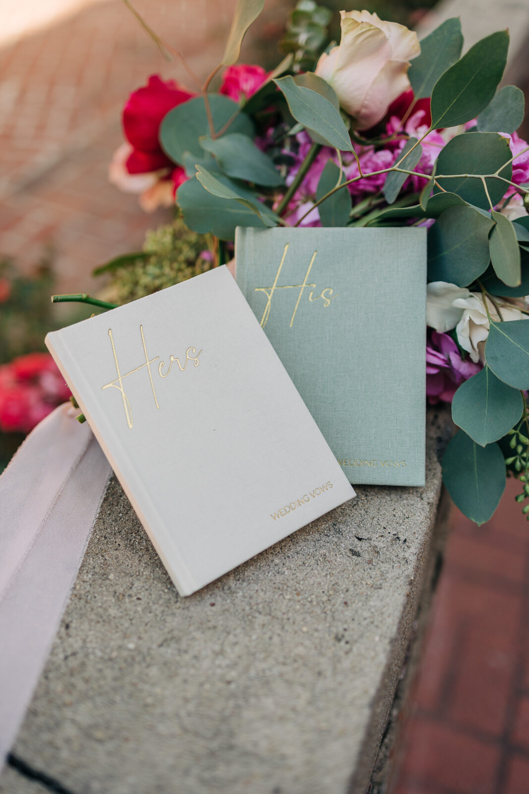 Sarah & Ethan"s wedding vow books in pale green and cream with gold lettering, surrounded by colorful flowers