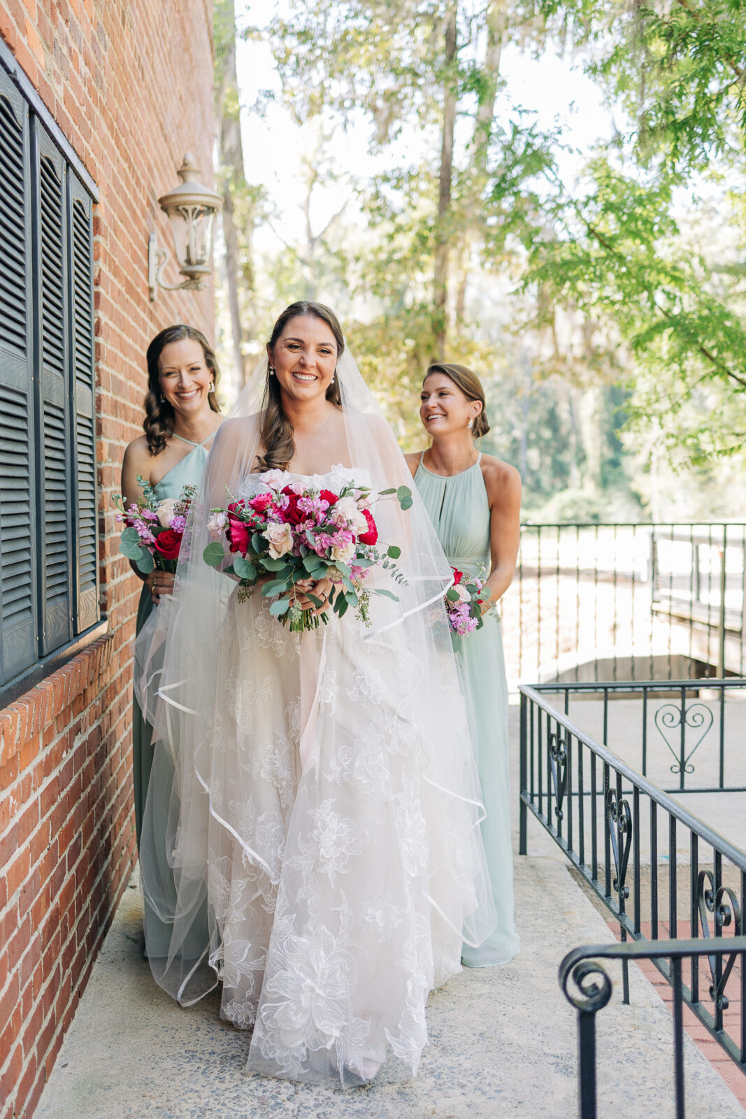 bride walking with bridesmaids in mint green dresses and holding a bright pink and red bouquet
