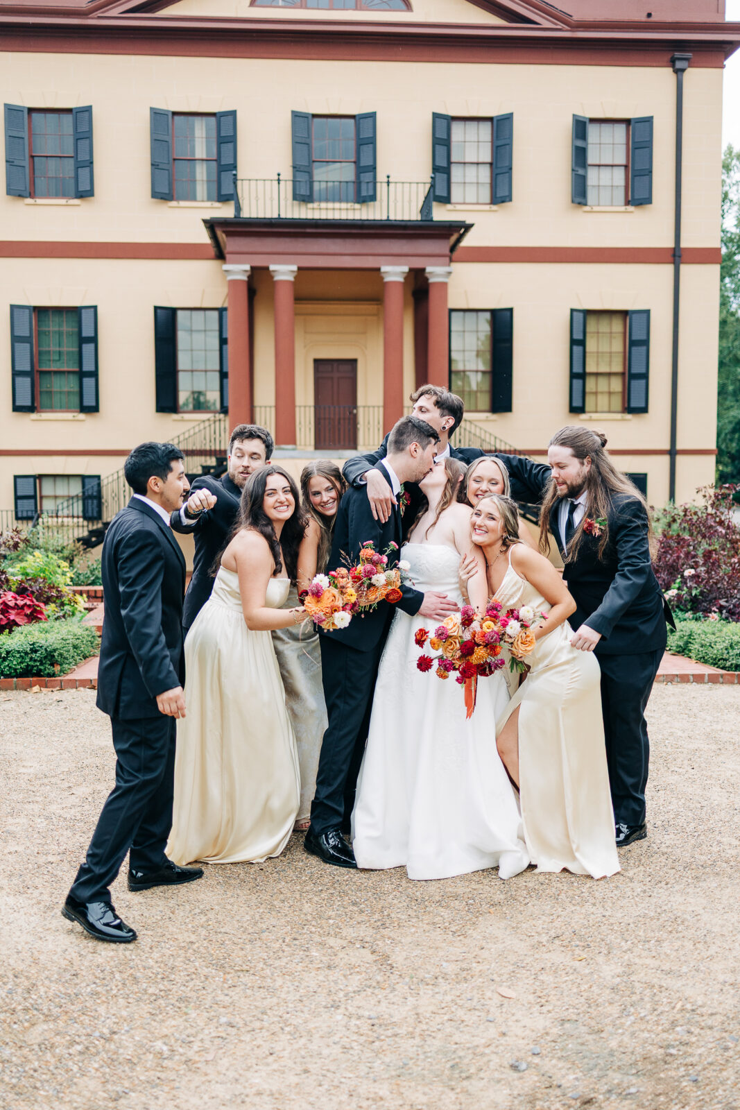 Fun wedding party portrait kissing the bride and groom in front of the historic Hampton-Preston Mansion