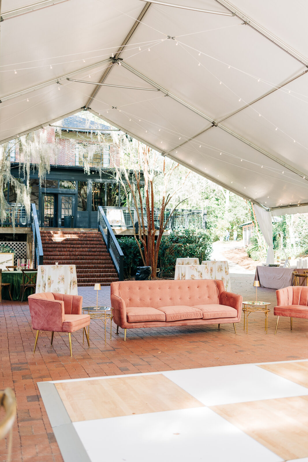Outdoor wedding tent reception interior with pink velvet furniture, string lights, and brick flooring at The Millstone at Adams Pond