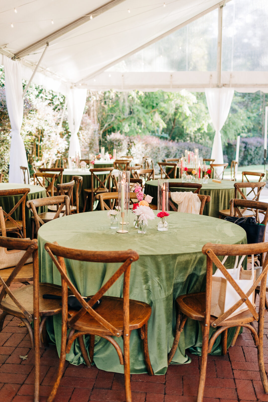 Tent reception table setting with green velvet linen, wood cross-back chairs, and small floral centerpieces in Columbia, SC