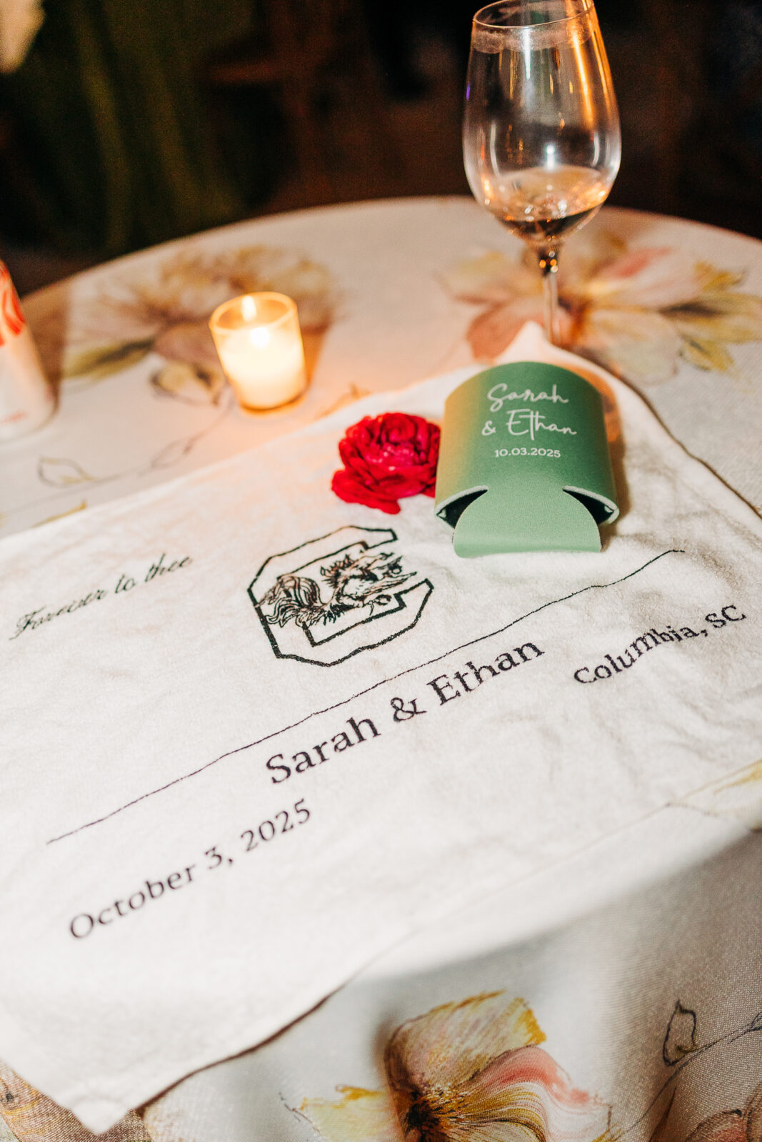 Personalized custom linen napkin with the couple's names, wedding date, and a koozie on a floral tablecloth at a Columbia, SC wedding reception