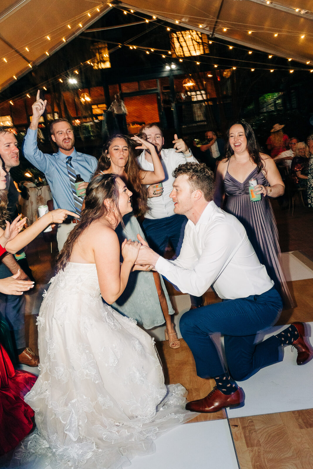 Fun, candid photo of the bride and groom laughing and dancing with their wedding guests under market lights at the reception