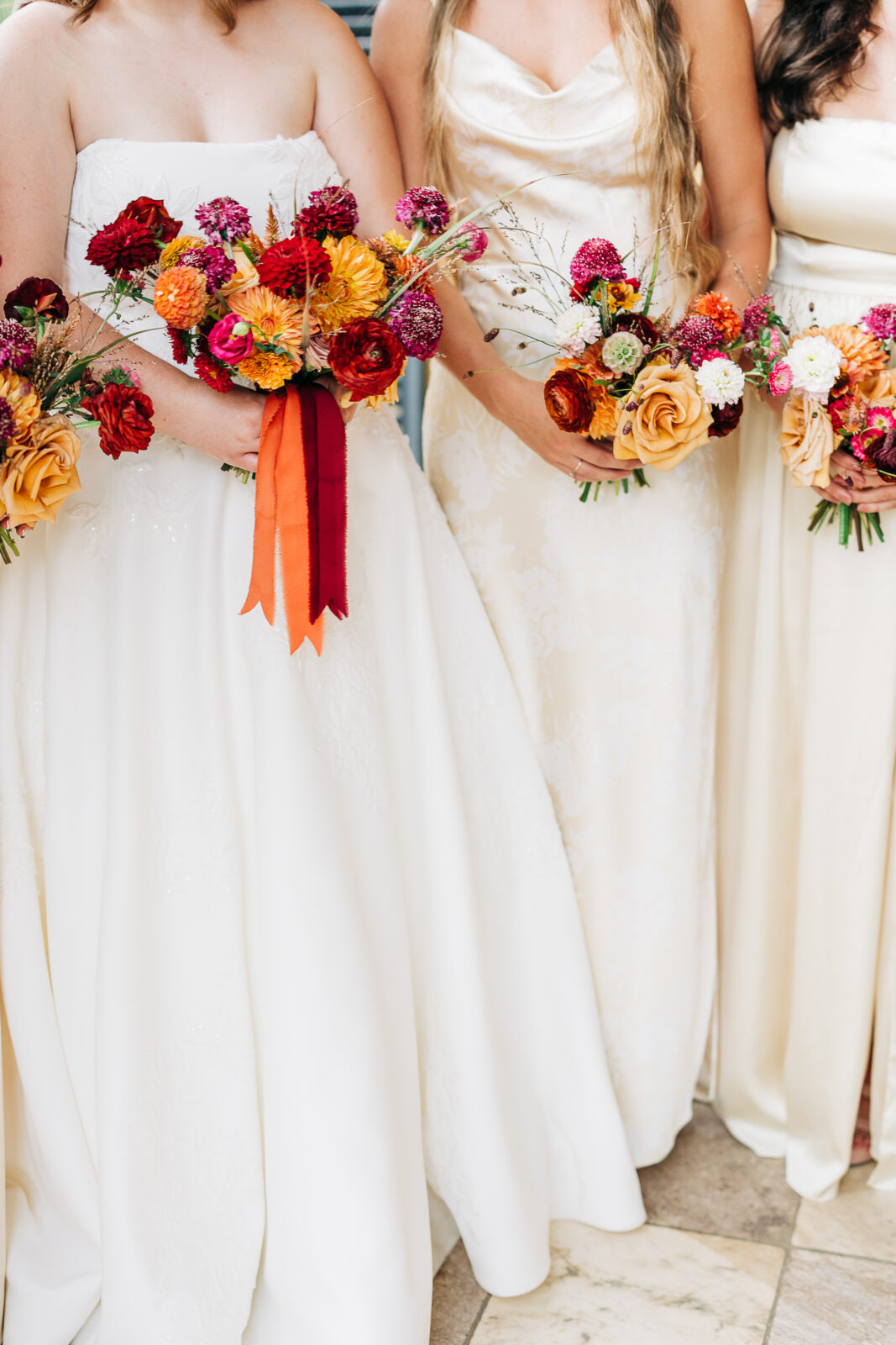 Bride and bridesmaids in ivory dresses holding vibrant red, orange, and pink bouquets at Hampton-Preston Mansion