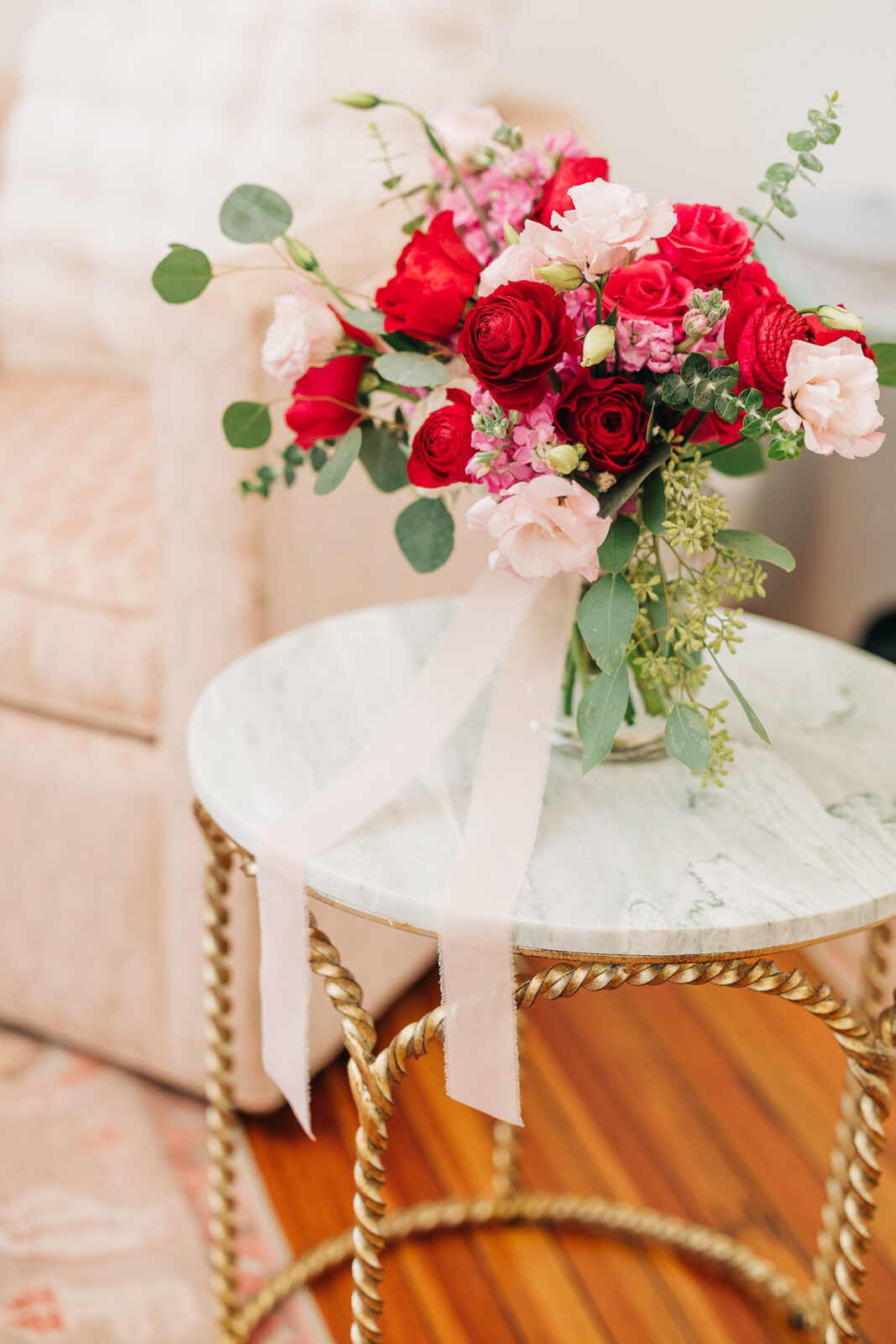 Detail shot of bride's vibrant red and pink bouquet on a gold and marble side table with ribbons