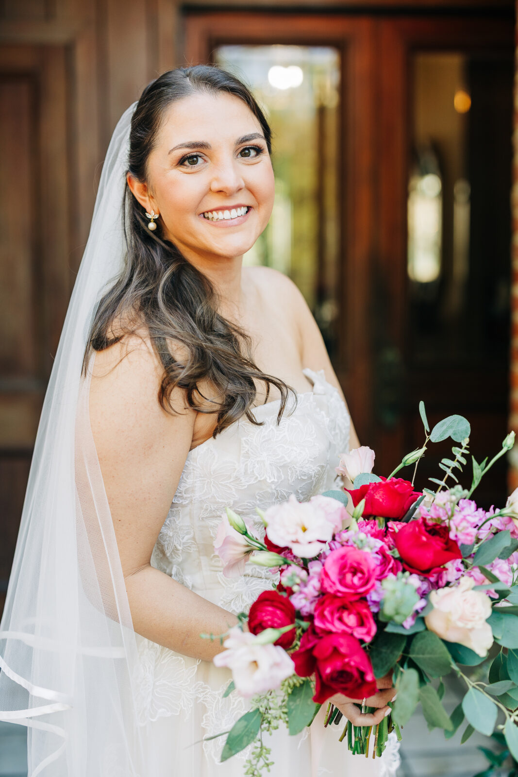 Bridal portrait, smiling bride, red and pink bouquet, veil, close-up