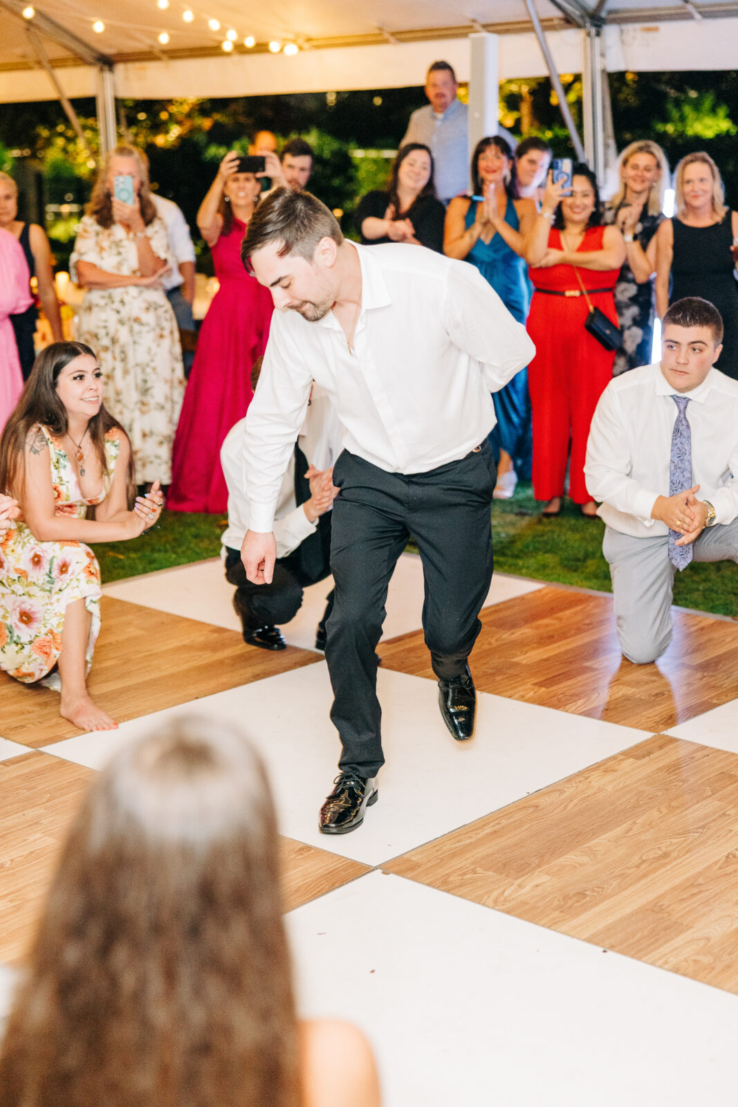 Groom and wedding guests dancing on a checkered dance floor under a white tent at a wedding reception in Columbia, SC, capturing the party atmosphere of the evening.