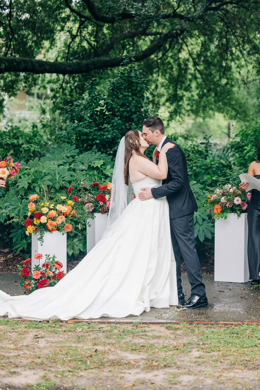 Bride and groom kiss during their wedding ceremony surrounded by colorful floral arrangements at Hampton-Preston Mansion and Gardens in Columbia, SC