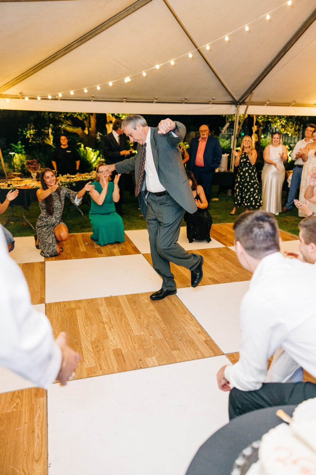 Joyful photo of a father of the bride or groom dancing energetically on a checkered wood floor under a tent with string lights at a wedding reception in Columbia, South Carolina.