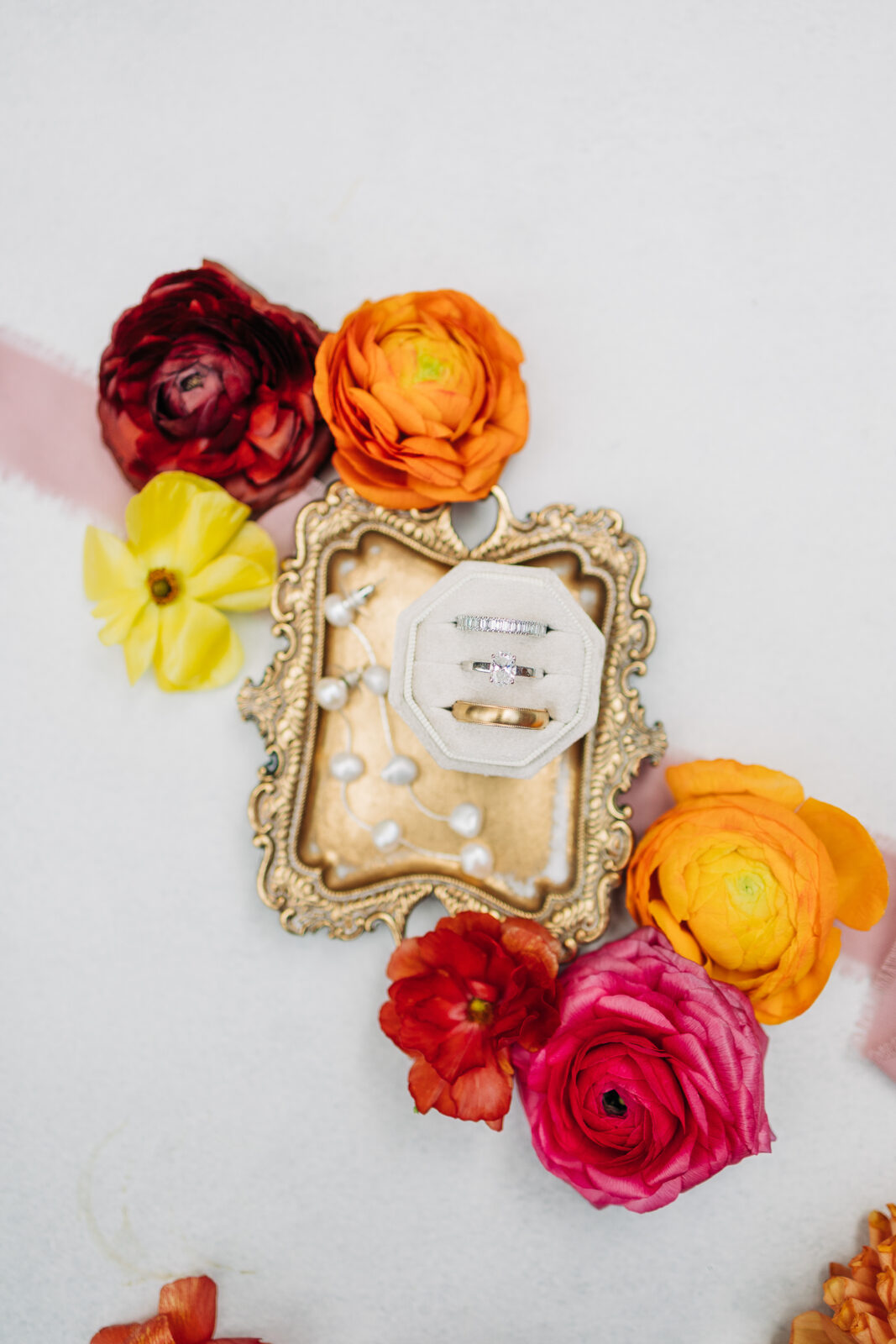 Styled flat lay with gold ring tray, wedding rings, and colorful ranunculus flowers in Columbia, SC