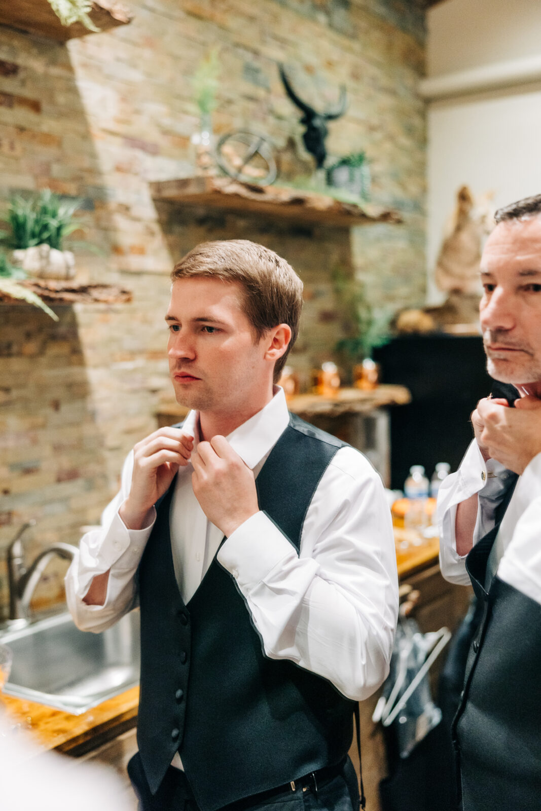 Groom getting ready, putting on white shirt and black vest at Oakbrook Farms