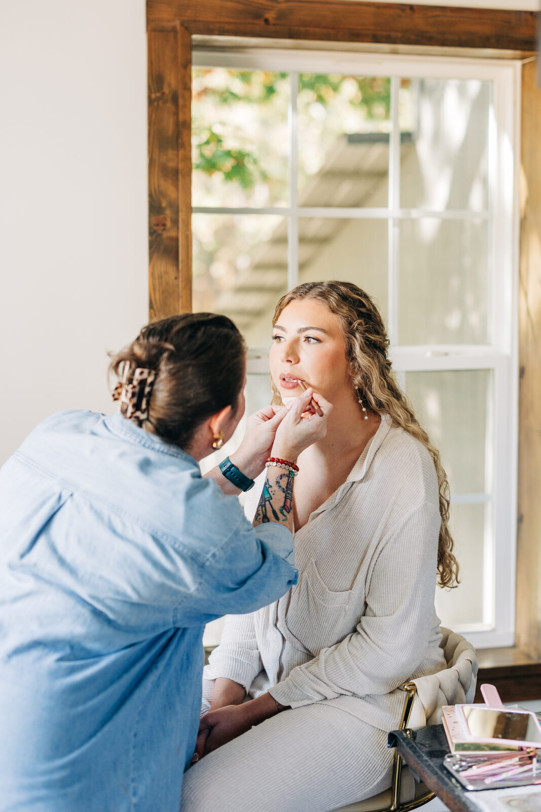 Bride getting makeup applied near a bright window before Oakbrook Farms wedding ceremony
