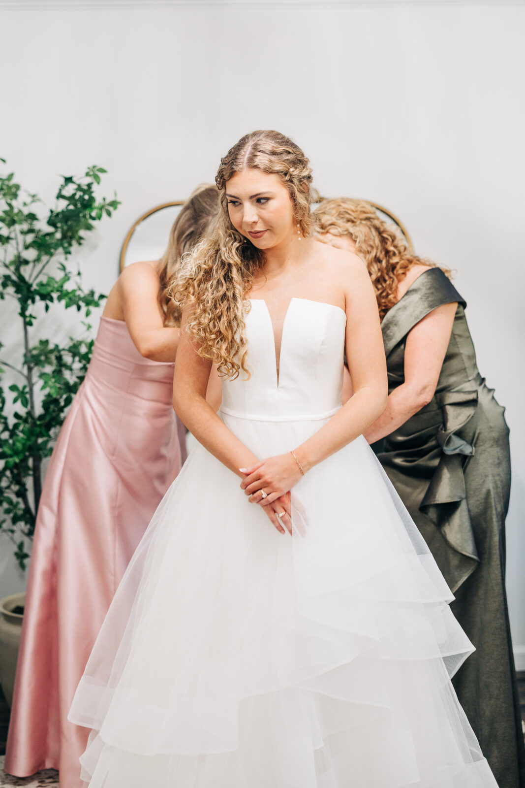 Beautiful bride in strapless wedding dress getting zipped up by bridesmaids at Oakbrook Farms