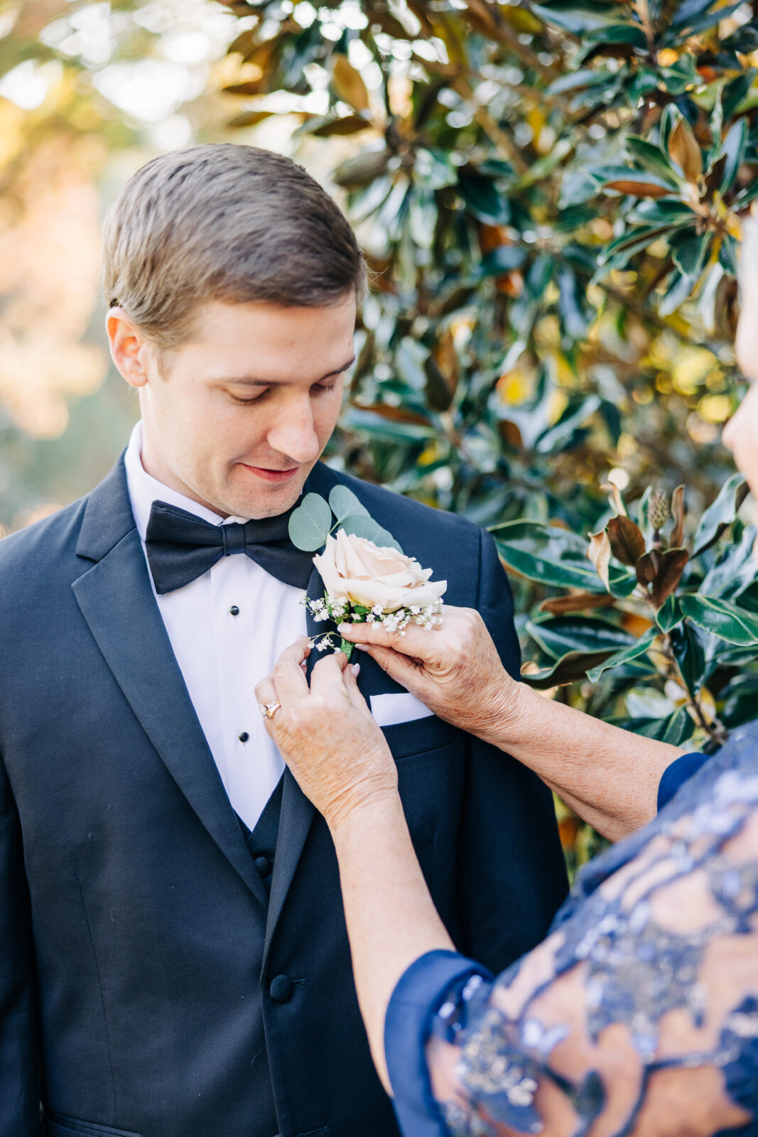 Groom having peach rose boutonniere pinned onto black tuxedo at Oakbrook Farms Wedding South Carolina