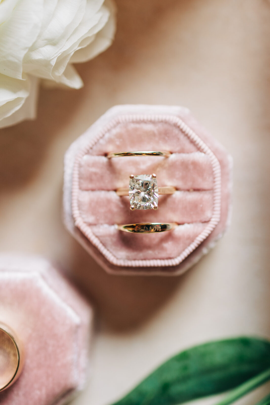 Close-up of radiant cut diamond engagement ring and gold wedding bands in pink velvet box
