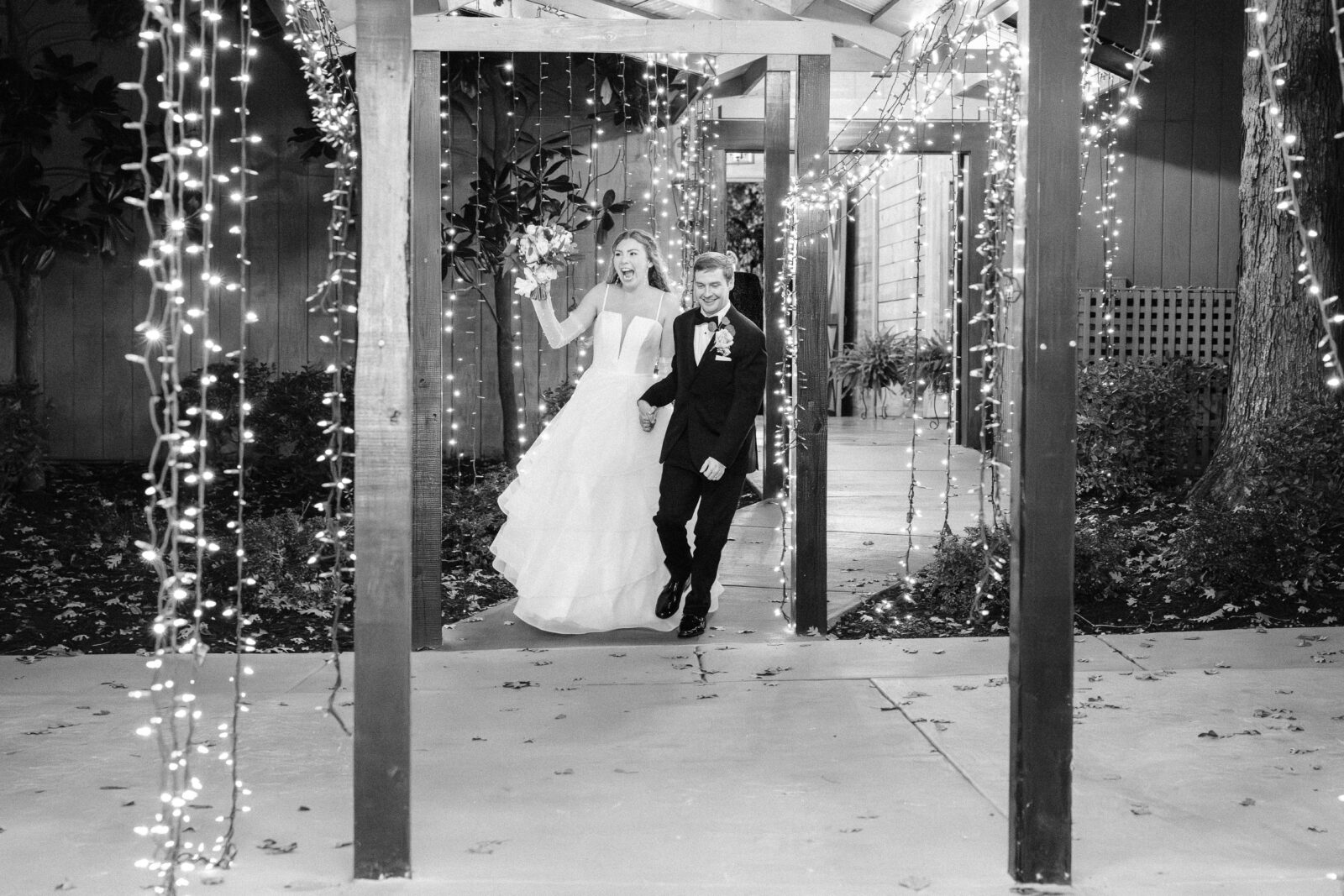 Black and white photo of Sarah and Thomas entering reception under twinkling lights at Oakbrook Farms
