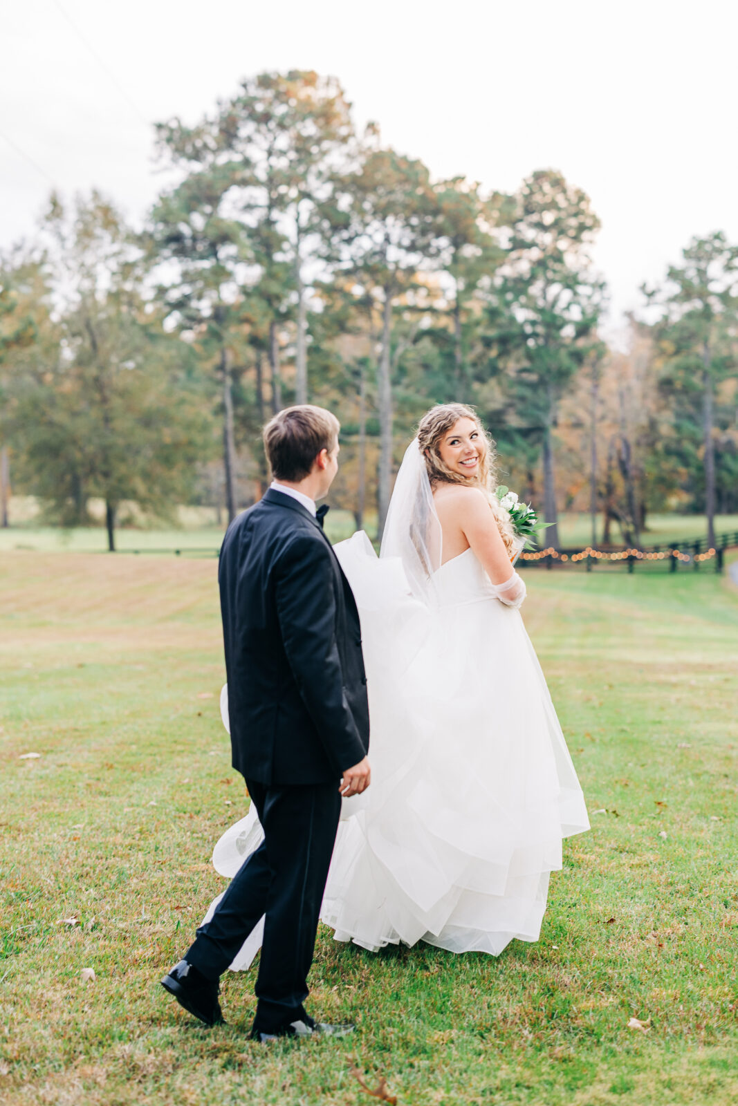 Joyful bride in white dress walking with groom on grassy lawn at Oakbrook Farms South Carolina