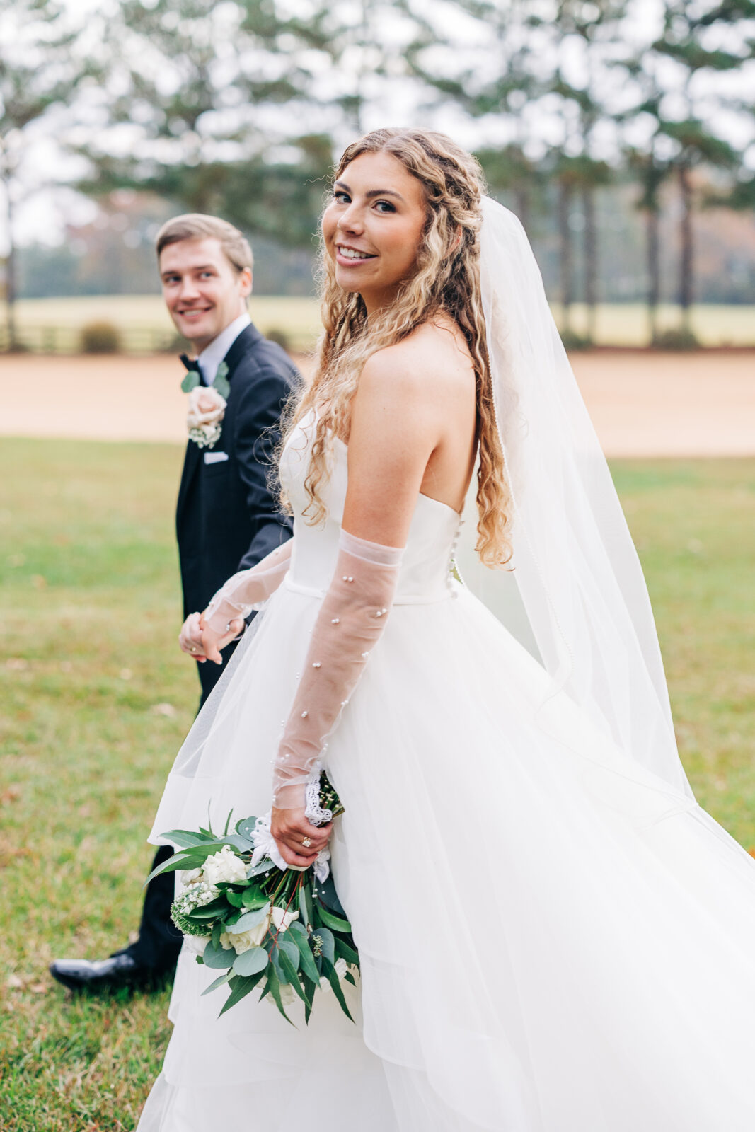 Beautiful bride with long curly hair and groom walking and holding hands at Oakbrook Farms SC