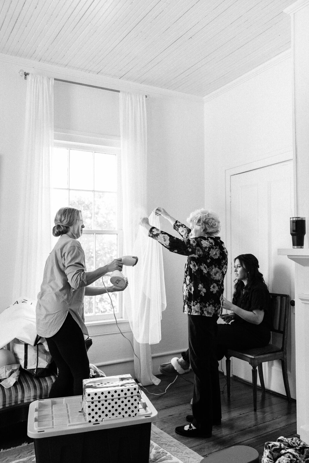 Two women steaming the bride's veil near a window in a bright room before the Hartley House Wedding South Carolina