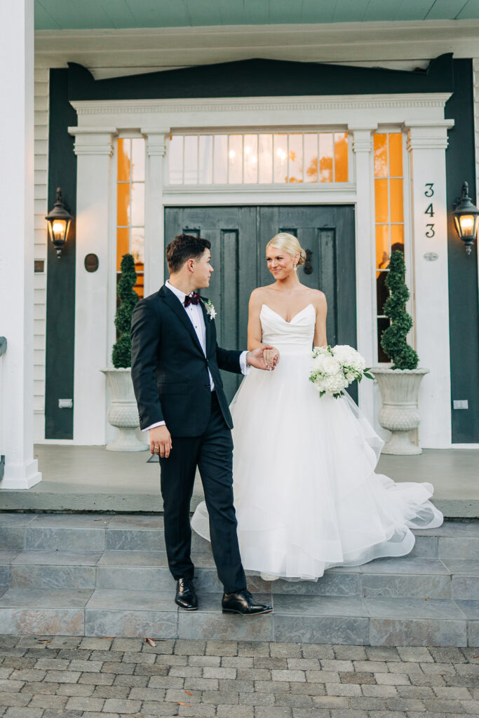 The bride and groom smiling as they descend the front steps of the beautiful white southern house, holding hands after their ceremony at the Hartley House