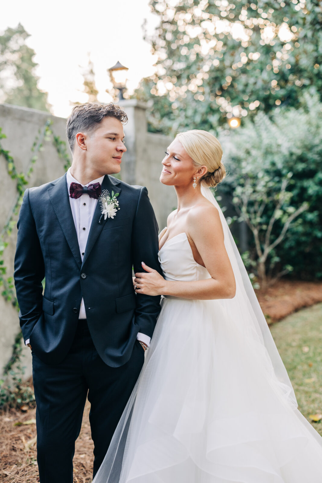 Outdoor portrait of the couple, the bride looking lovingly at the groom as he rests his hand in his pocket, taken against a vine-covered wall at the Hartley House Wedding South Carolina