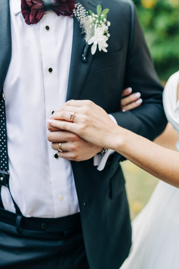 showcasing the wedding rings and the groom's dark suit and maroon bow tie at the Hartley House Wedding South Carolina