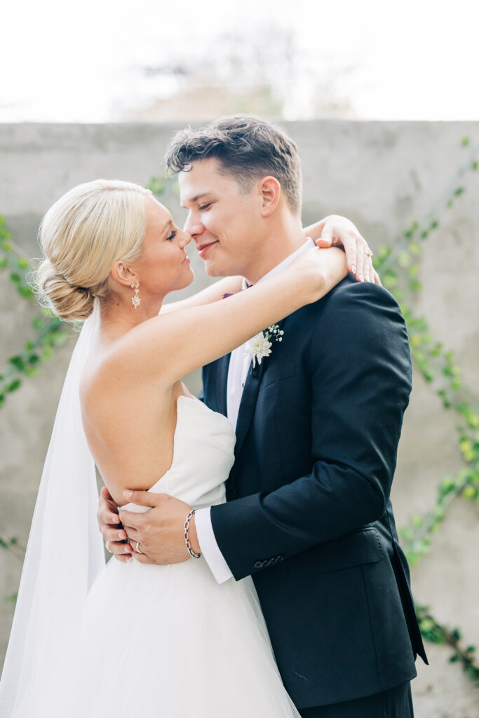 Romantic close-up of the bride and groom embracing, nose to nose, against the backdrop of the vine-covered stone wall