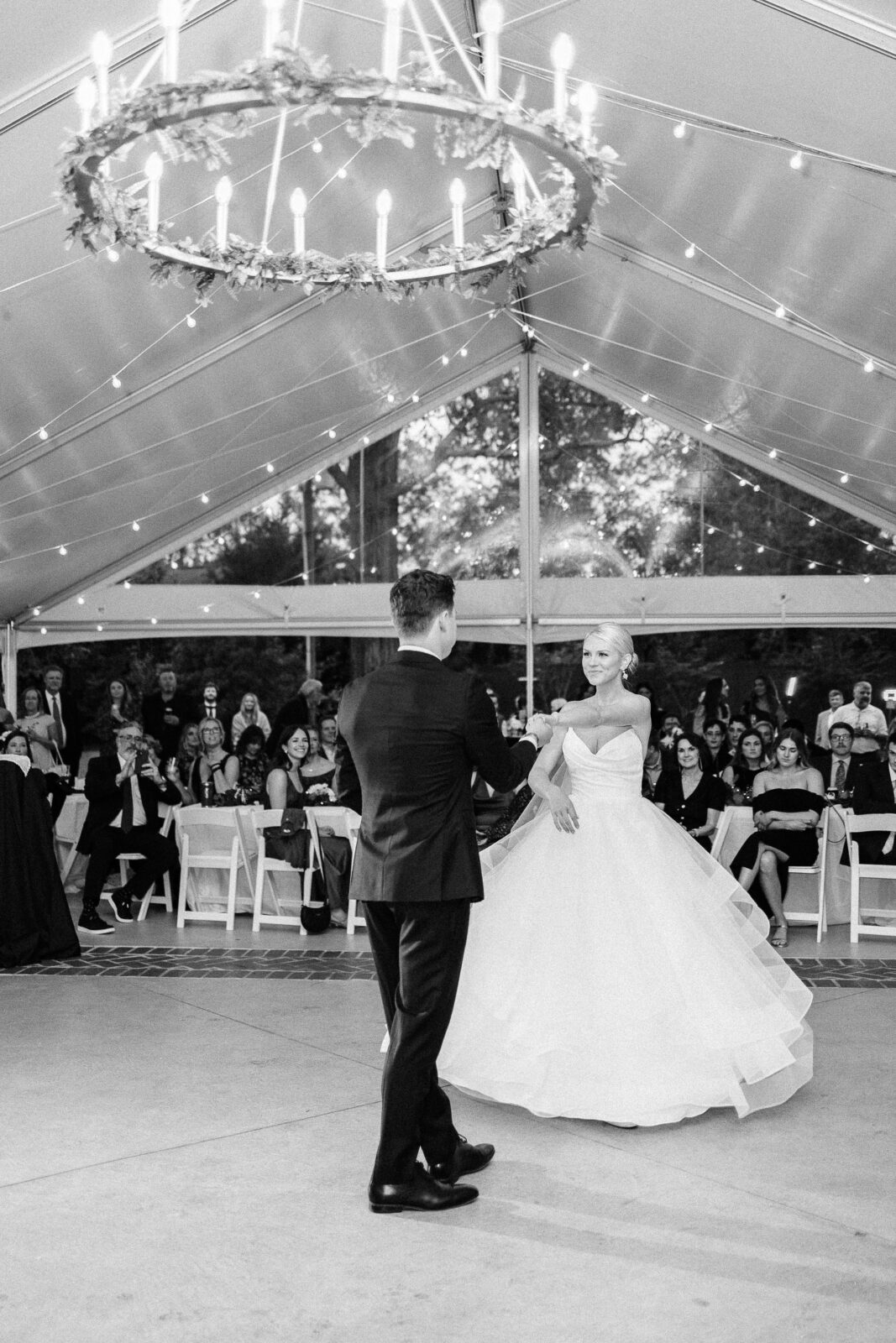 Black and white photo of the bride and groom enjoying their first dance, looking into each other's eyes under the twinkling lights and chandelier at the Hartley House Wedding South Carolina receptio
