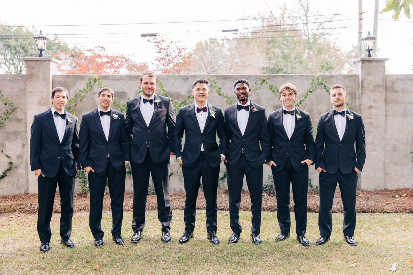 Close-up of the groom's classic black tuxedo and deep red velvet bow tie, with the white flower boutonnière pinned to the lapel, ready for the Hartley House Wedding South Carolina wedding