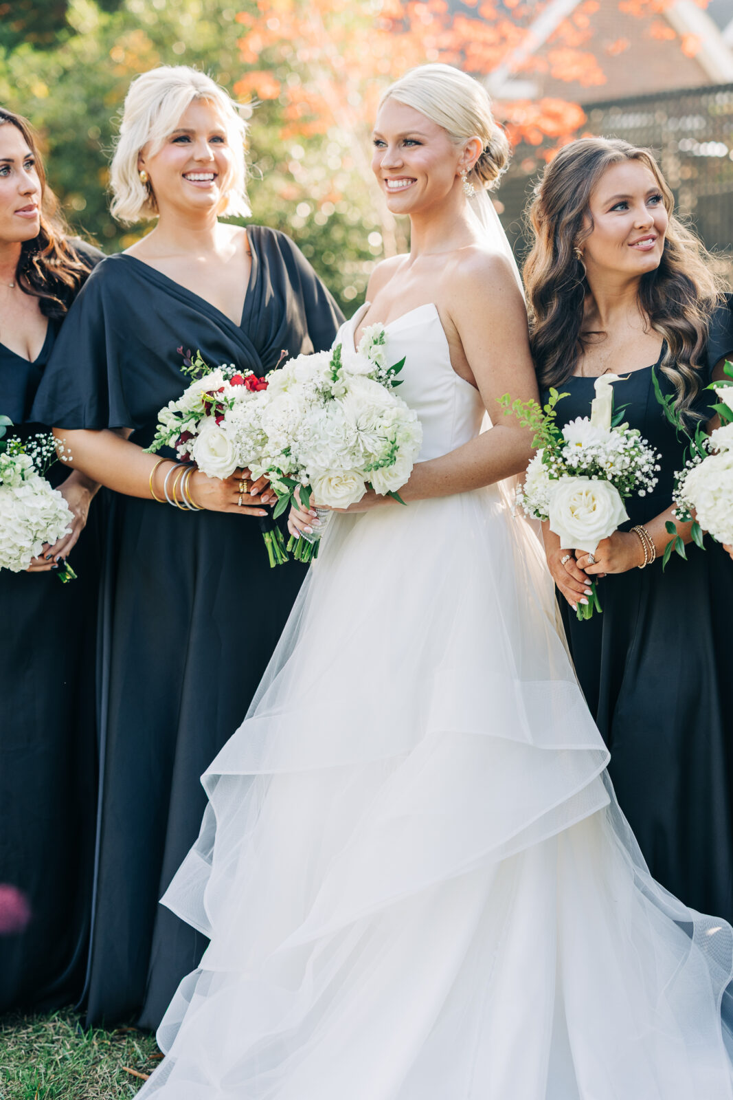 Close-up of the bride and three bridesmaids smiling while holding white hydrangea and rose bouquets outdoors at the Hartley House Wedding South Carolina venue