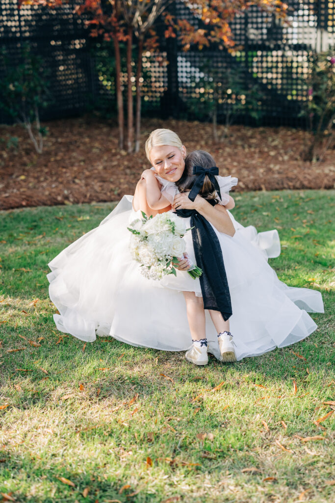 The bride and her five bridesmaids in long black dresses walking arm-in-arm and smiling while crossing the manicured lawn before the ceremony at the Hartley House Wedding South Carolina
